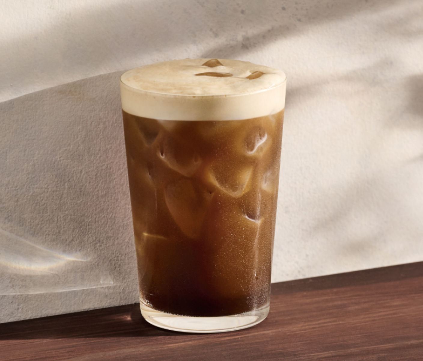 Un aerocano dans un grand verre servi avec de la glace. Une mousse légère descend en vagues et se fond graduellement à l’espresso foncé au fond du verre. 